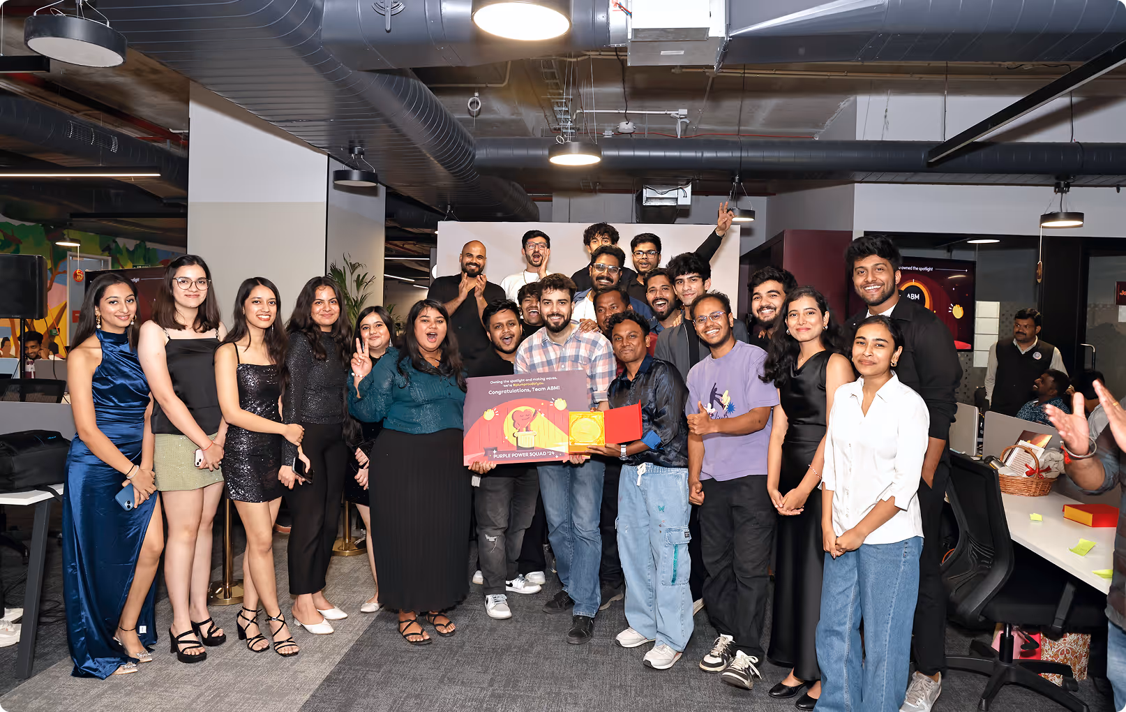 A diverse group of smiling young adults in office attire posing indoors, holding a congratulatory award plaque.